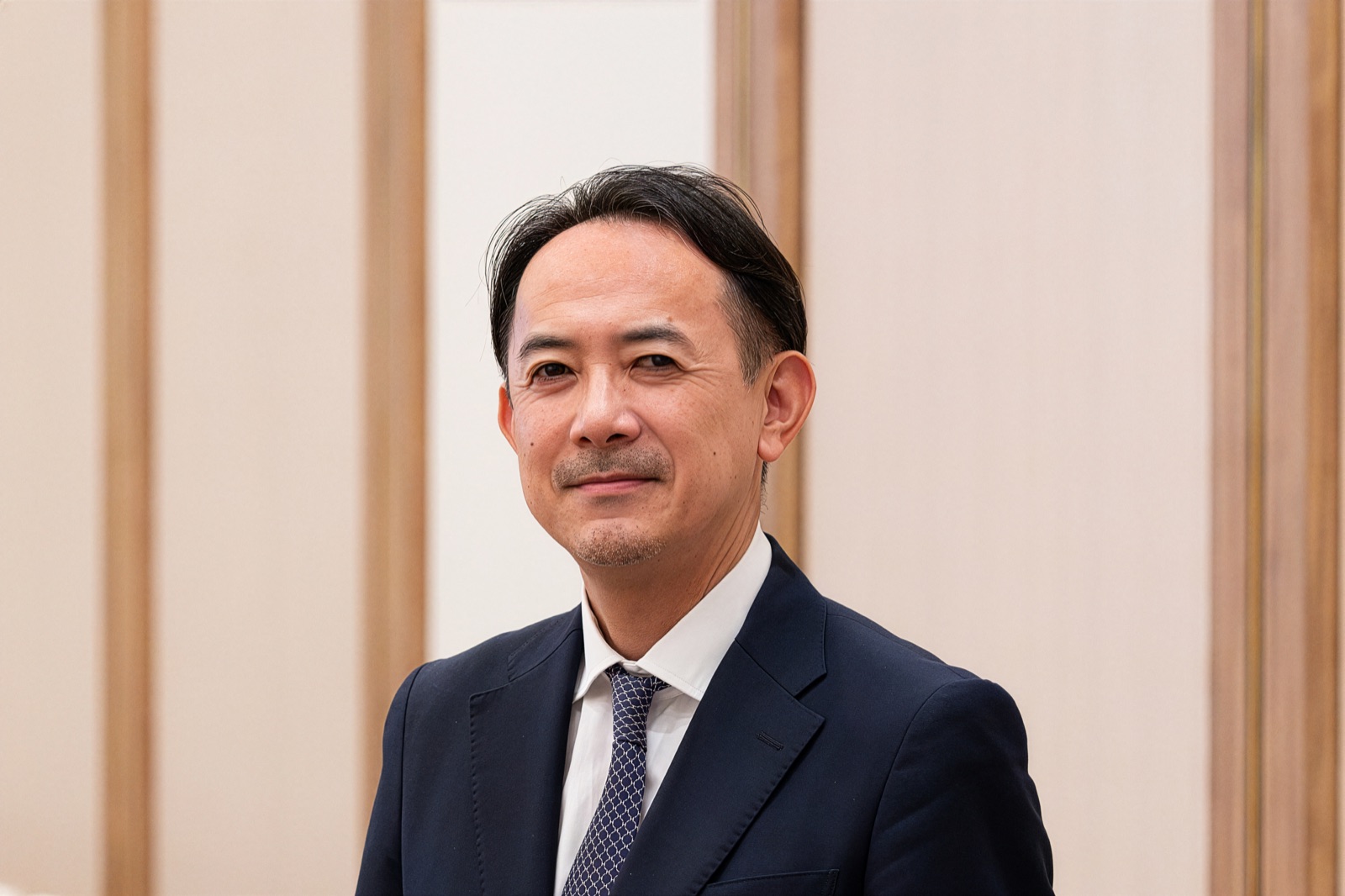 川邊健太郎 プロフィール写真（スーツ・木目背景・笑顔）