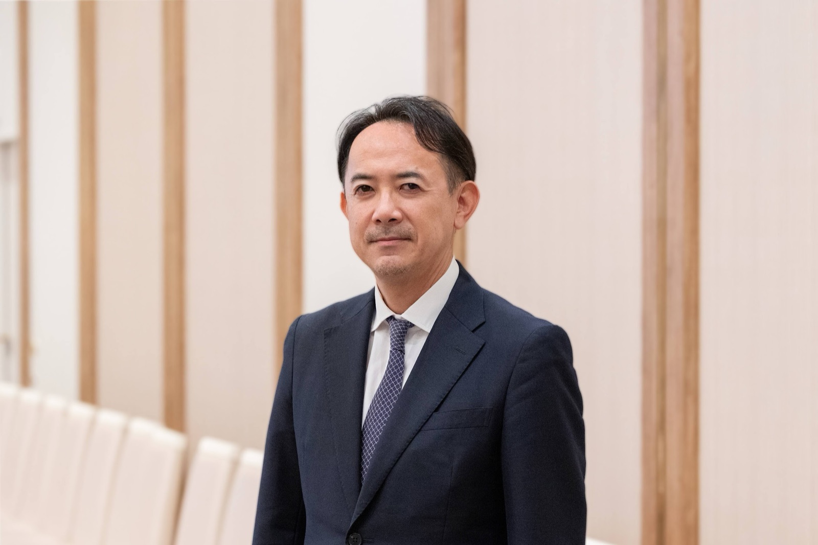 川邊健太郎 プロフィール写真（スーツ・木目背景）